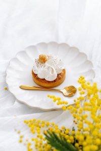 Elegant dessert with whipped cream and a golden spoon, accompanied by vibrant yellow mimosa flowers.