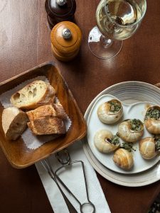 Gourmet dining setup featuring escargot, bread, and white wine on a rustic table.