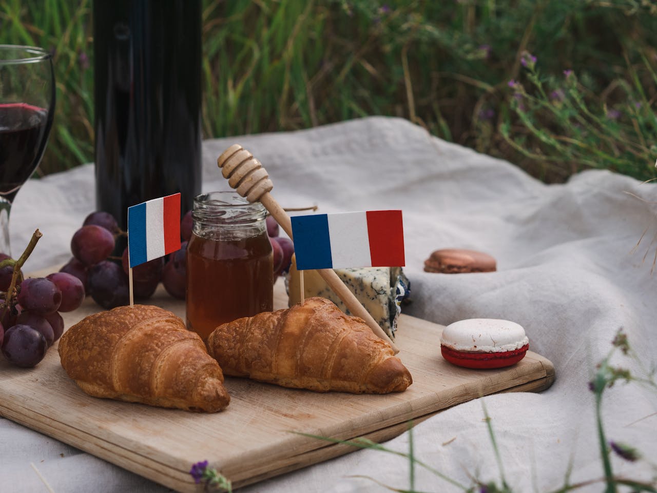 A delightful French picnic setup with croissants, cheese, grapes, and red wine outdoors.