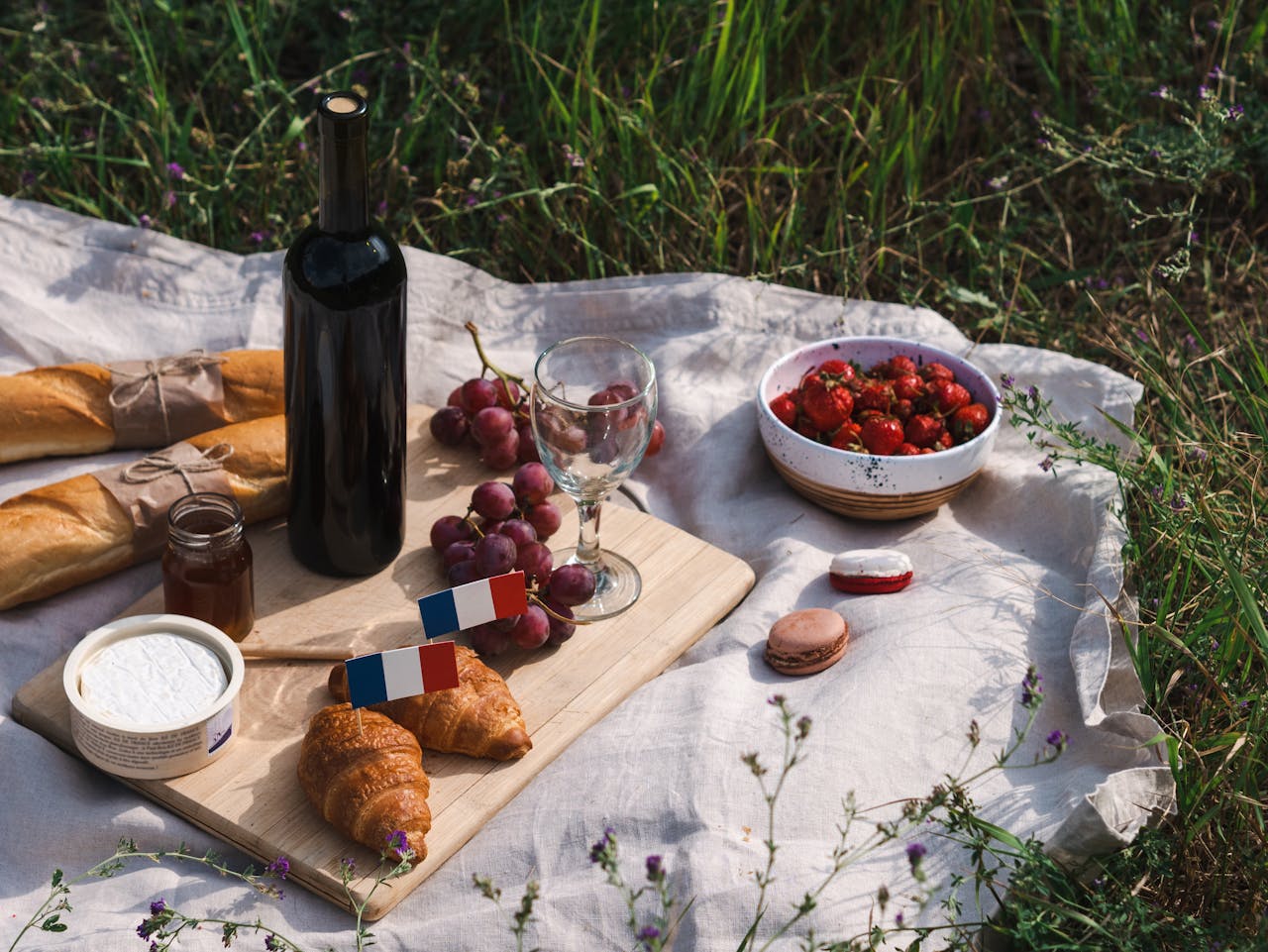 A delightful outdoor French picnic setup featuring baguettes, wine, and a variety of fresh foods.